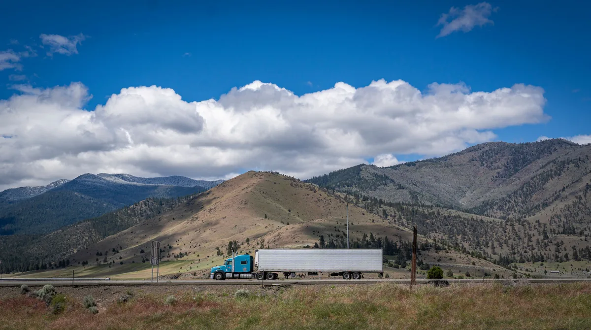 Blue semi-truck traveling on a mountain highway, shown as illustrative stock photography